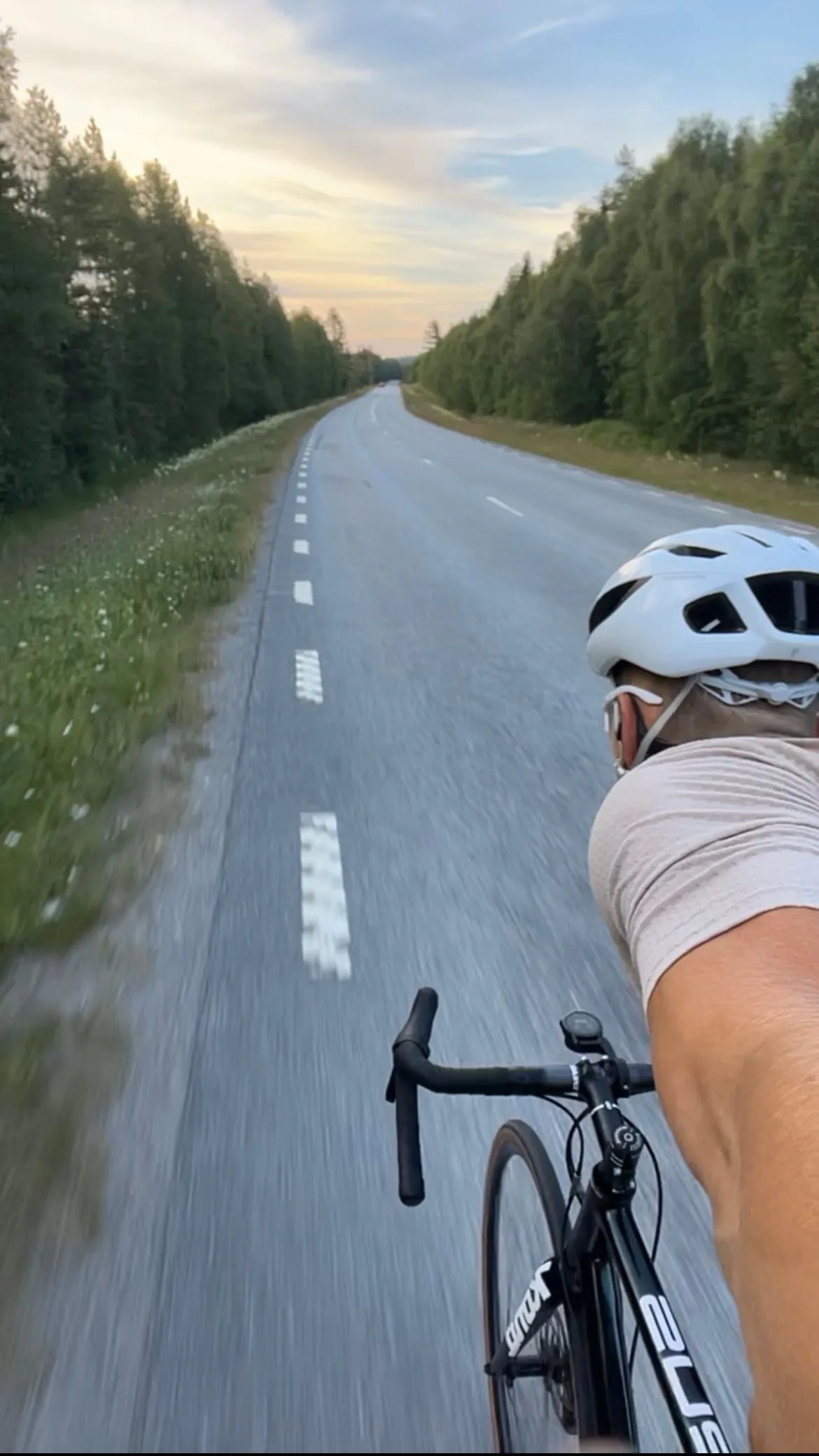 Riding along an empty forest-lined road in northern Sweden at dusk, seen over the handlebars